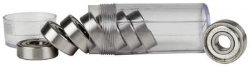 A transparent cylindrical container, open with several Sushi Chrome ABEC 7 Skateboard Bearings, spills some while others remain. Additional precision bearings are visible beside it, and the separated cap lies nearby.