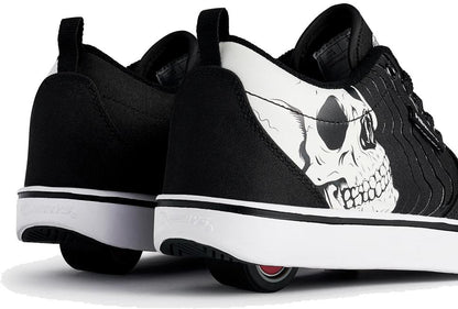 A close-up of Heelys Pro 20 PRNT Glow Boys Shoes in black and white, featuring a glow-in-the-dark skull graphic on the side and low-profile wheels in the heels.