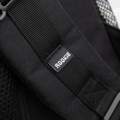 Close-up of a black fabric strap on the Rookie Skatepack Classic 78 25L Backpack by Rookie, featuring a small tag with "ROOKIE" in white text. Mesh material is partially visible on the side, showcasing the thoughtful design of this 25-liter backpack.