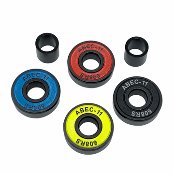 Four vibrant skateboard bearings from the Logic ABEC 11 Multi Colour Scooter Bearings - 4 Pack are displayed on a white background, highlighting their premium quality. The set includes bearings in striking red, yellow, blue, and black colors. Accompanying these high-performance essentials for your ride are two black cylinder spacers.